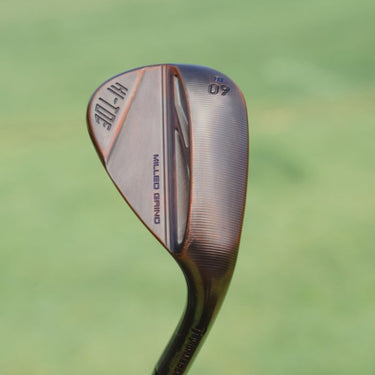 TaylorMade Hi-Toe 3 Wedge lifestyle image on a grass background, showing the sole of the club and the back of the club in the aged copper finish. 